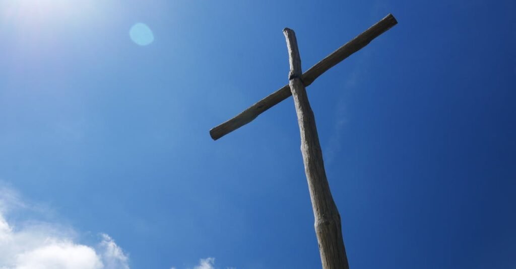 Low angle view of a wooden cross under a clear blue sky with bright sunlight.
